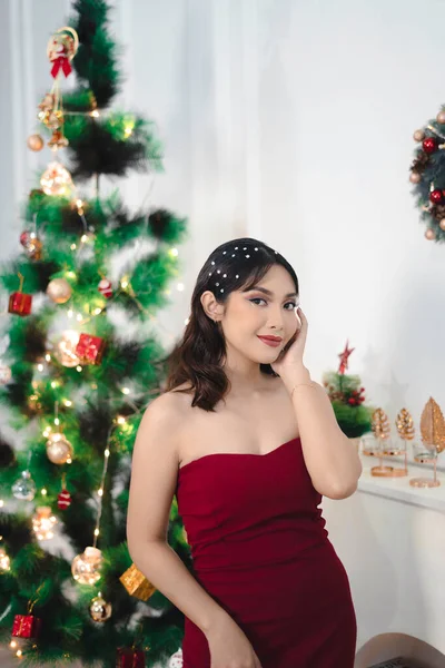 赤いガウンを着たかなり若い女の子の肖像画 カメラで笑顔 室内装飾されたクリスマスのリビングルームに立って — ストック写真