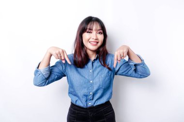 Excited Asian woman wearing blue shirt pointing down at the copy space, isolated by white background