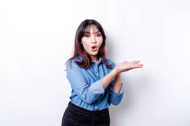 Shocked Asian woman wearing blue shirt pointing at the copy space beside her, isolated by white background