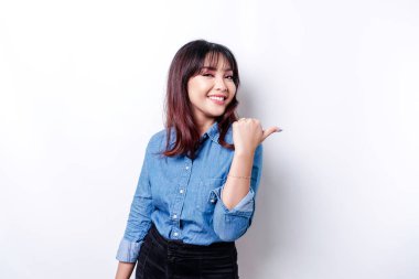 Excited Asian woman wearing blue shirt pointing at the copy space beside her, isolated by white background