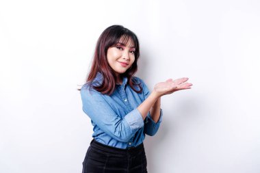 Excited Asian woman wearing blue shirt pointing at the copy space beside her, isolated by white background