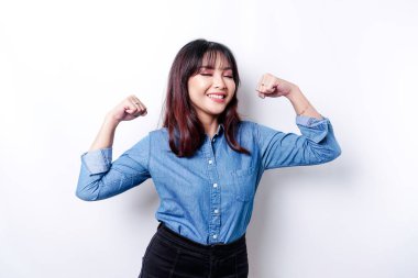 Excited Asian woman wearing a blue shirt showing strong gesture by lifting her arms and muscles smiling proudly