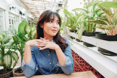 Thoughtful Asian woman keeps hand on chin looks pensively above dressed in blue shirt poses thinks about future