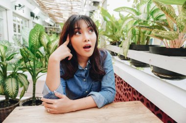 A thoughtful young woman dressed in blue shirt and holding her chin while looking aside