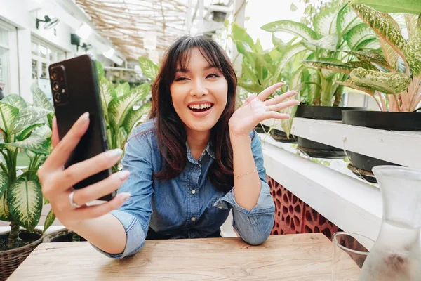 A happy Asian woman in a restaurant, wearing a blue shirt and holding her phone