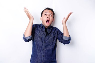 Shocked Asian man wearing blue shirt pointing at the copy space on top of him, isolated by white background