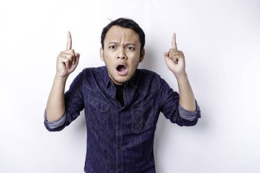 Shocked Asian man wearing blue shirt pointing at the copy space on top of him, isolated by white background