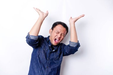 Shocked Asian man wearing blue shirt pointing at the copy space on top of him, isolated by white background