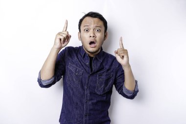 Shocked Asian man wearing blue shirt pointing at the copy space on top of him, isolated by white background