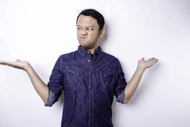 A portrait of an Asian man wearing a blue shirt looks so confused between choices, isolated by a white background