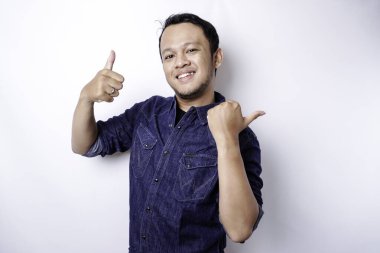 Excited Asian man wearing blue shirt pointing at the copy space beside him, isolated by white background