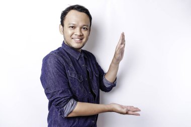 Excited Asian man wearing blue shirt pointing at the copy space beside him, isolated by white background