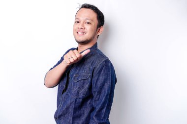 Excited Asian man wearing blue shirt pointing at the copy space beside him, isolated by white background