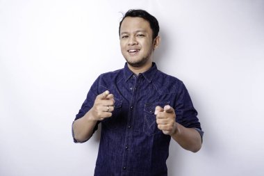 Young Asian man wearing blue shirt standing over isolated white background pointing fingers to camera with happy face. Good energy and vibes.