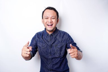 Young Asian man wearing blue shirt standing over isolated white background pointing fingers to camera with happy face. Good energy and vibes.
