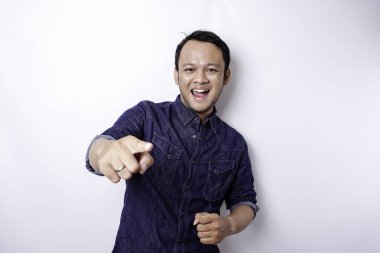 Young Asian man wearing blue shirt standing over isolated white background pointing fingers to camera with happy face. Good energy and vibes.