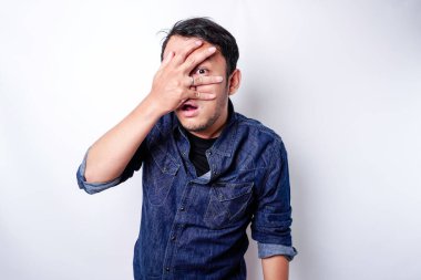 Funny obvious peeking Asian man in blue shirt isolated on white background.