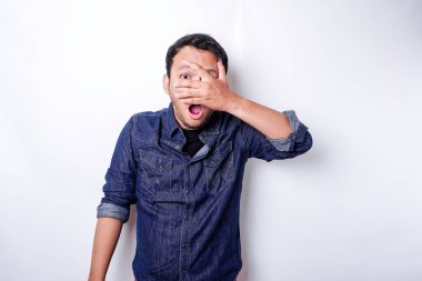 Funny obvious peeking Asian man in blue shirt isolated on white background.