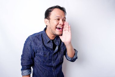 Young handsome man wearing a blue shirt shouting and screaming loud with a hand on his mouth. communication concept.