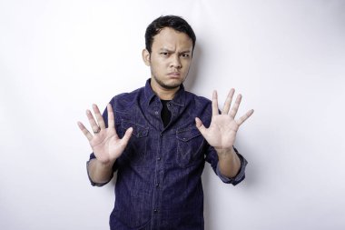 Handsome Asian man wearing blue shirt with hand gesture pose of stop or prohibition with copy space