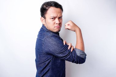 Excited Asian man wearing a blue shirt showing strong gesture by lifting his arms and muscles smiling proudly