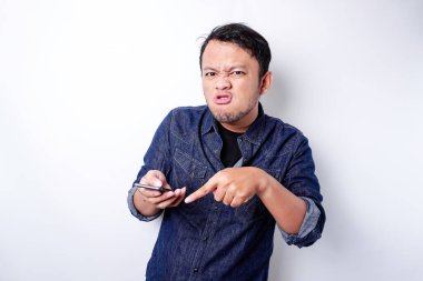 The angry and mad face of Asian man in blue shirt holding his phone isolated white background.