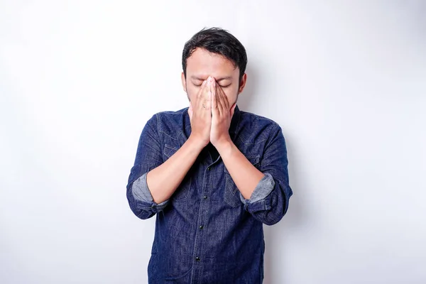 A portrait of an Asian man wearing a blue shirt isolated by white background looks depressed