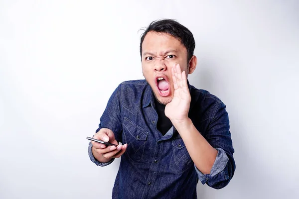 The angry and mad face of Asian man in blue shirt holding his phone isolated white background.