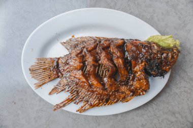 Grilled gourami or Gurame bakar with red barbeque sauce on a white plate