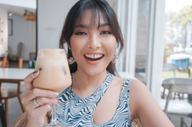 Yakın plan kız kahve içiyor. Dudaklarında kahve köpüğü var ve gülümsüyor. Sabah kapuçinosunun tadını çıkarıyor..