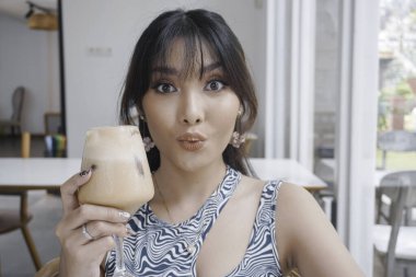 Yakın plan kız kahve içiyor. Dudaklarında kahve köpüğü var ve gülümsüyor. Sabah kapuçinosunun tadını çıkarıyor..