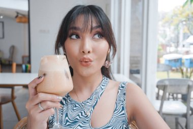 Yakın plan kız kahve içiyor. Dudaklarında kahve köpüğü var ve gülümsüyor. Sabah kapuçinosunun tadını çıkarıyor..