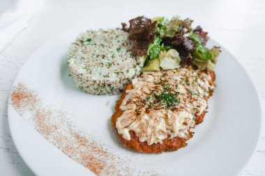 Chicken parmigiana with handmade tomato sauce with herb rice and salad on a white plate.
