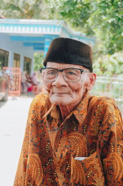A portrait of an old Asian man wearing batik shirt and glasses