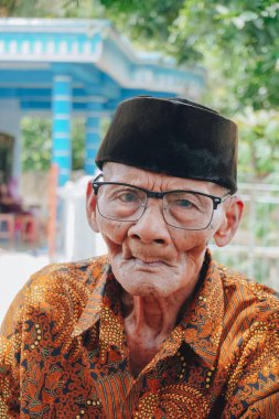 A portrait of an old Asian man wearing batik shirt and glasses