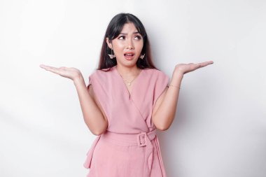 A thoughtful young Asian woman is wearing pink blouse holding her phone and looks confused, isolated by white background