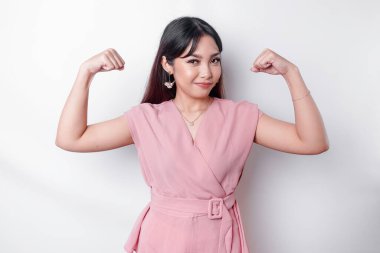 Excited Asian woman wearing a pink blouse showing strong gesture by lifting her arms and muscles smiling proudly
