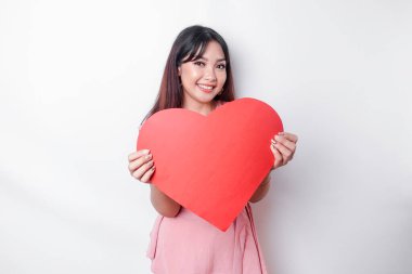 A portrait of a happy Asian woman wearing a pink blouse, holding a red heart-shaped paper isolated by white background