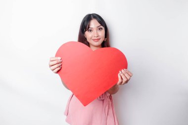 A portrait of a happy Asian woman wearing a pink blouse, holding a red heart-shaped paper isolated by white background