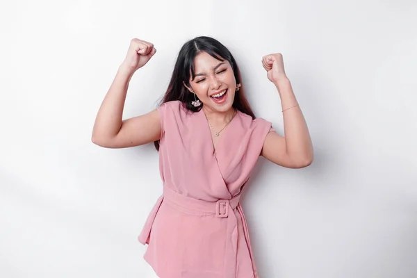 A young Asian woman with a happy successful expression wearing pink blouse isolated by white background