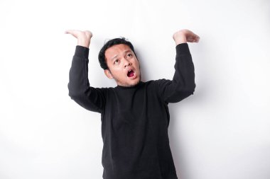 Shocked Asian man wearing black shirt pointing at the copy space on top of him, isolated by white background