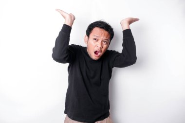 Shocked Asian man wearing black shirt pointing at the copy space on top of him, isolated by white background