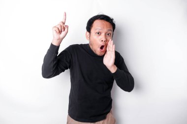 Shocked Asian man wearing black shirt pointing at the copy space on top of him, isolated by white background