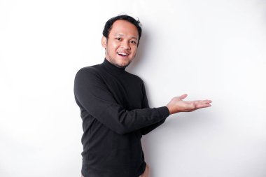 Excited Asian man wearing black shirt pointing at the copy space beside him, isolated by white background
