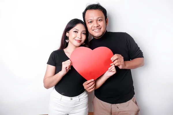 A young Asian couple smiling and holding red heart-shaped paper, isolated by white background