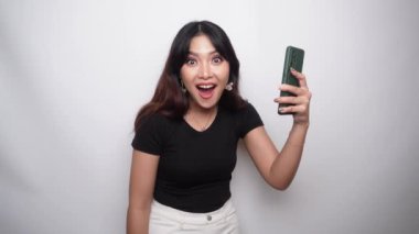 A portrait of a happy Asian woman dressed in black shirt and holding her phone, isolated by white background