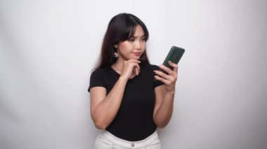 A thoughtful young woman in black shirt and holding her chin with phone on hand isolated by white background