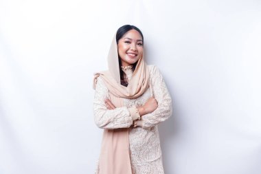 Portrait of a confident smiling Asian Muslim woman wearing hijab standing with arms folded and looking at the camera isolated over white background