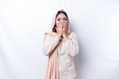Oops! Surprised young Asian Muslim woman covering mouth with hands and staring at camera while standing against white background