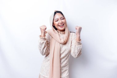 Mutlu bir ifadeyle genç bir Asyalı Müslüman kadın beyaz arka planla izole edilmiş tesettür takıyor.